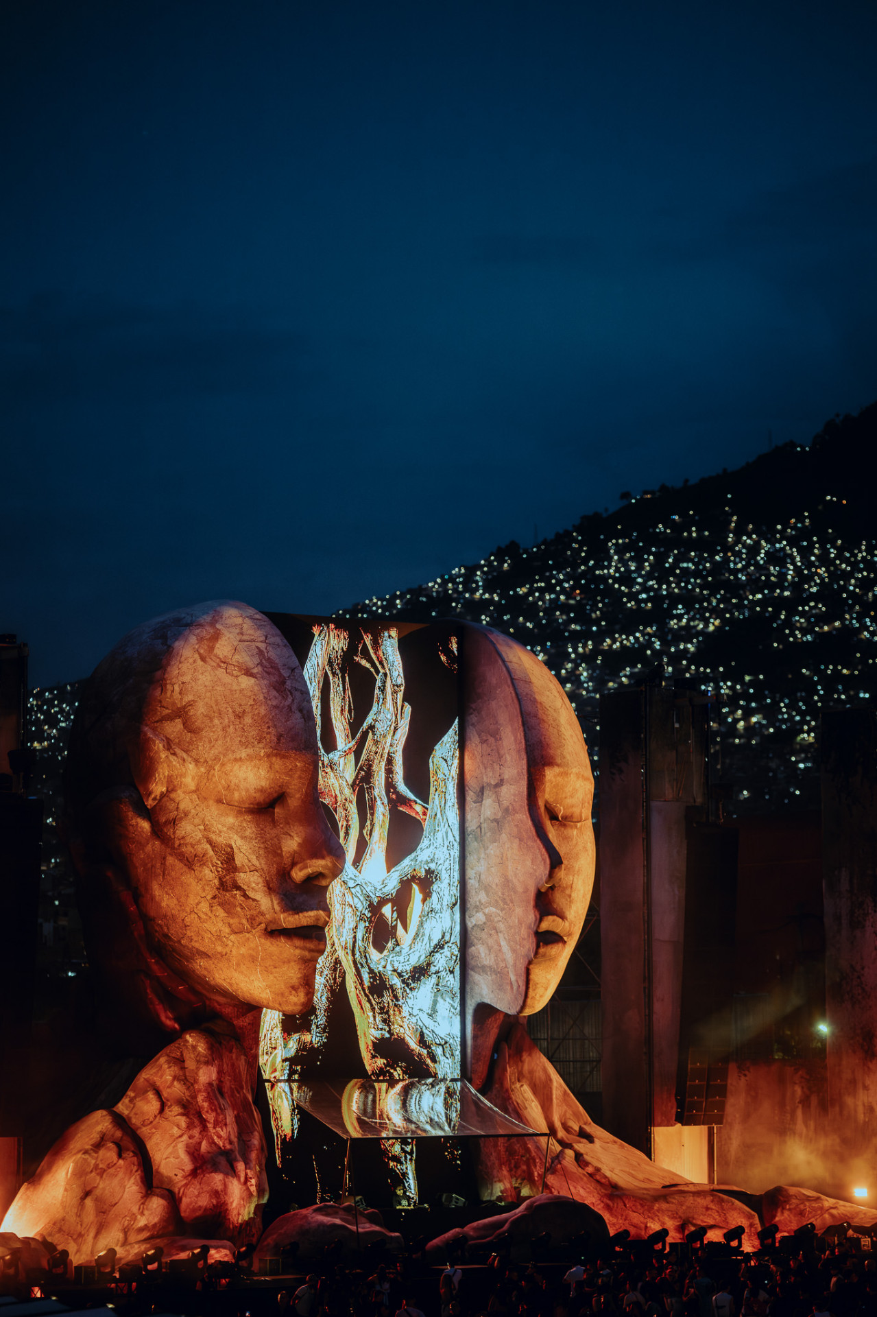 Twin sculptural faces of the CORE main stage at dusk, city lights behind