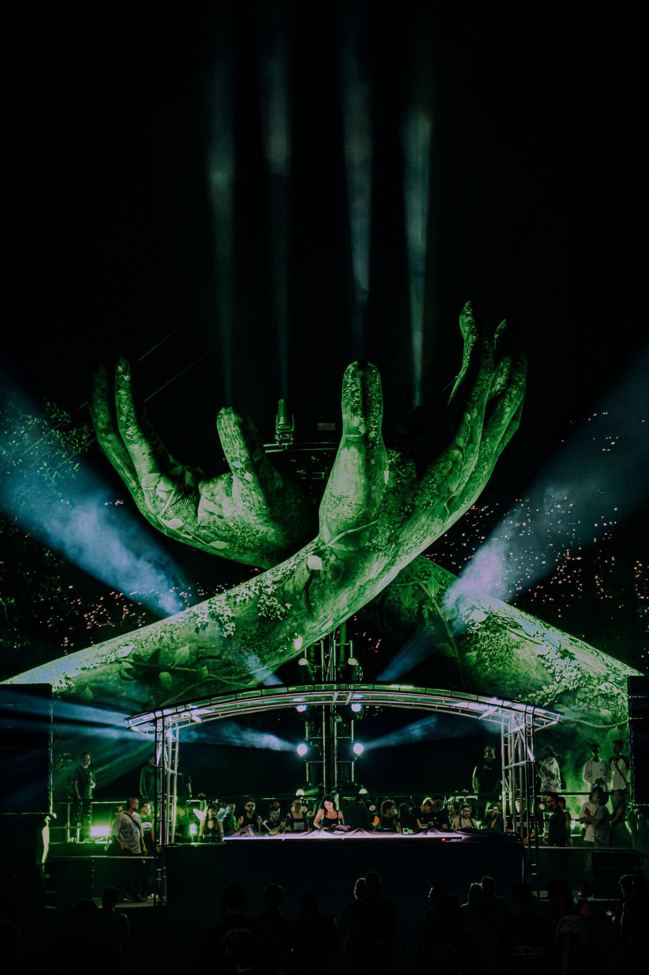Hands raised in the crowd under green stage lighting